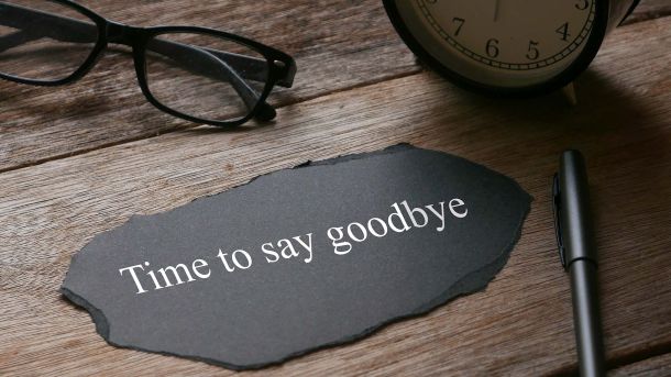 The words 'Time to say b=goodbye' on a piece of fabric laying on a wooden desk