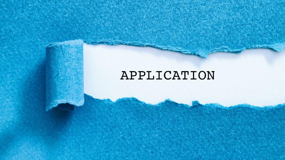 A strip of blue paper being peeled away to reveal the word 'application'.